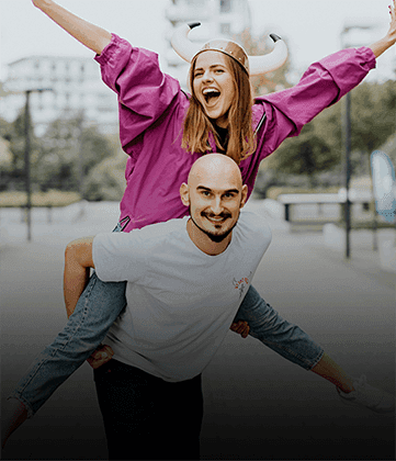Smiling woman in a horned helmet rides on a man’s back with arms raised in joy