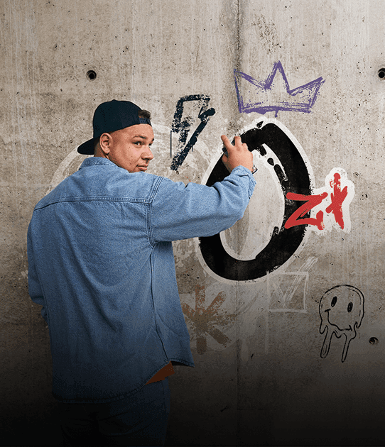 Mężczyzna w czapce z daszkiem i jeansowej kurtce maluje graffiti na betonowej ścianie