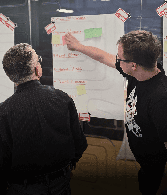 Two men discuss ideas written on a workshop board