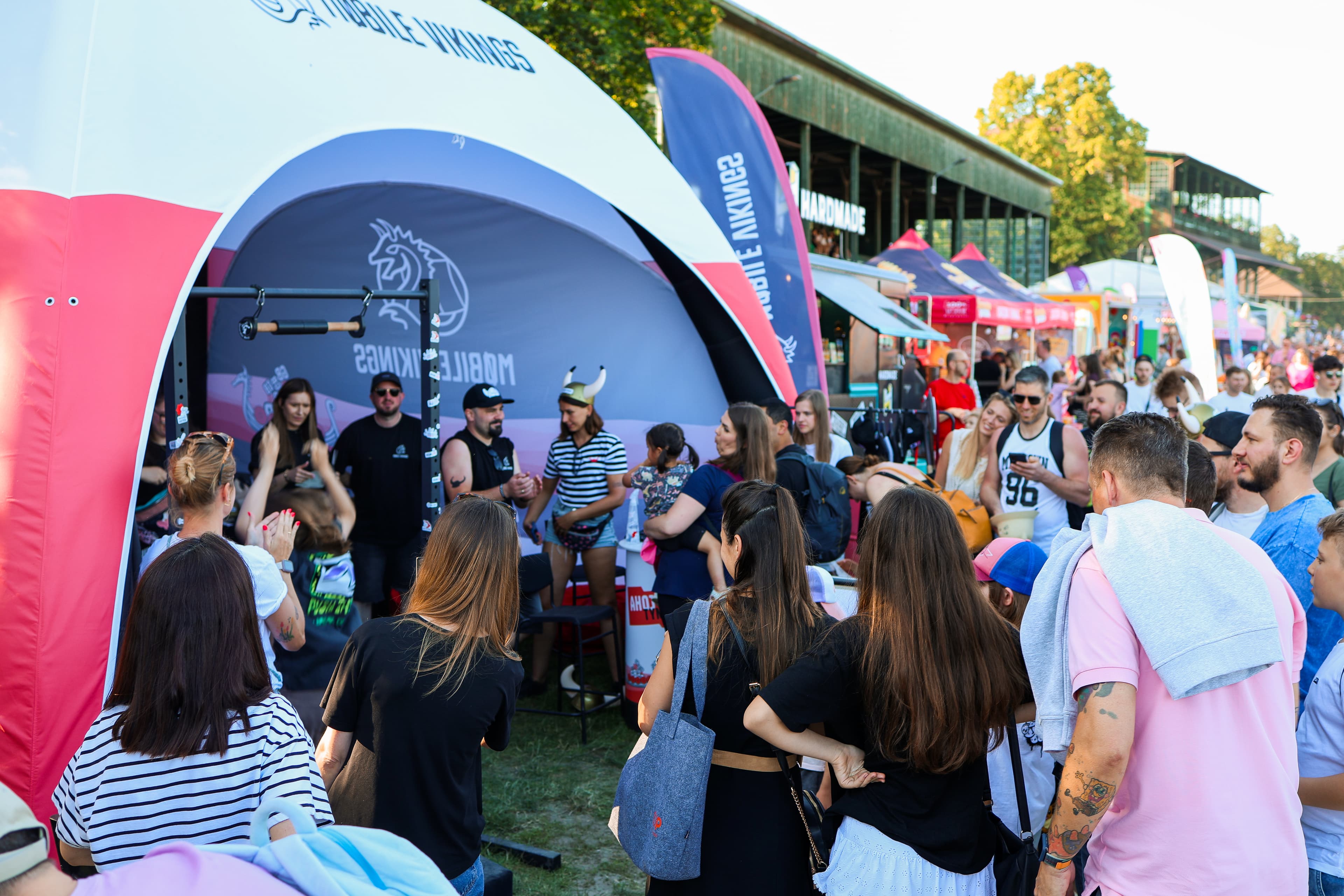 namiot festiwalowy a przy nim dużo ludzi, w tym osoba wisząca na drążku