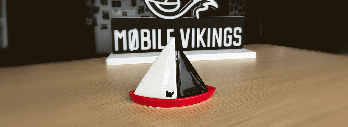 Ceramiczna figurka łódki stoi na stole przed podświetlanym logo Mobile Vikings