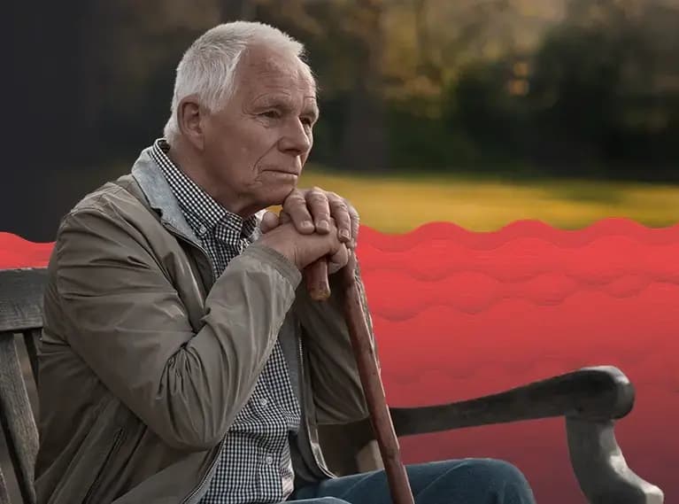 Starszy mężczyzna siedzi zamyślony na ławce i opiera ręce na lasce