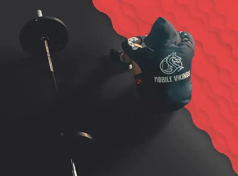 Osoba w bluzie Mobile Vikings siedzi obok sztangi, na głowie ma kaptur