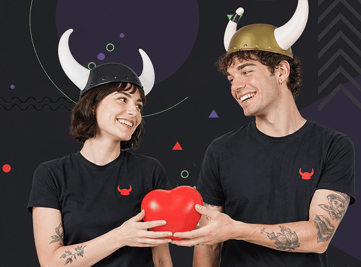 Smiling couple wearing Viking helmets holds a heart-shaped balloon and looks at each other