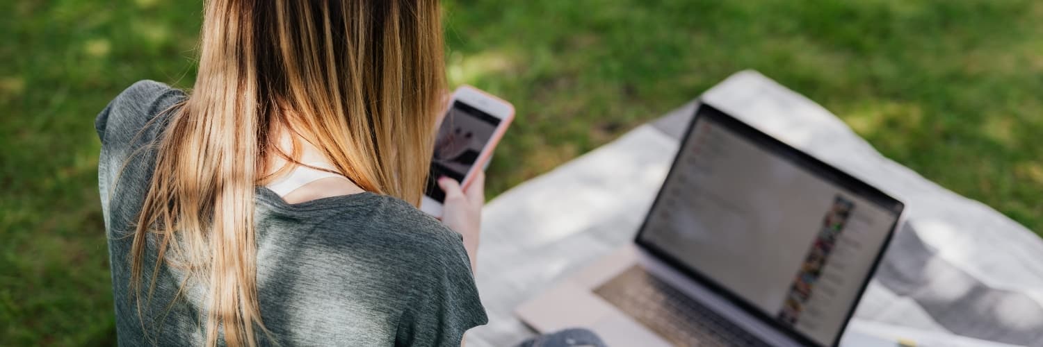 dziewczyna trzyma telefon na pikniku a w tle laptop