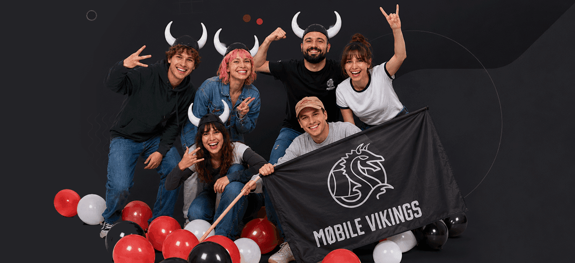 Group wearing horned helmets poses among balloons with a Mobile Vikings flag, flashing rock hand signs
